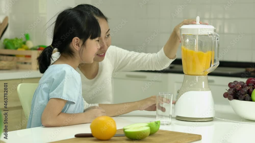 Asian family cooking at home. Pregnant woman and daughter making orange juice smoothie with electric blender in kitchen room at home. Family making healthy drinks while being quarantine at home. Asian family cooking at home. Pregnant woman and daughter making orange juice smoothie with electric blender in kitchen room at home. Family making healthy drinks while being quarantine at home.