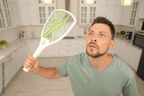 Slika na platnu Man with electric fly swatter in kitchen. Insect killer