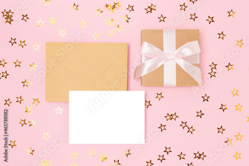 Layout of empty paper card, envelope and gift box with ribbon on a pink background with stars confetti. © rorygezfresh