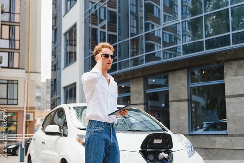 A handsome young man is charging his modern electric car.