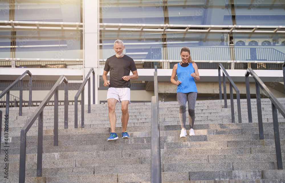 Motivated couple, middle aged man and woman in sportswear running up a flight of stairs while training together outdoors in the city