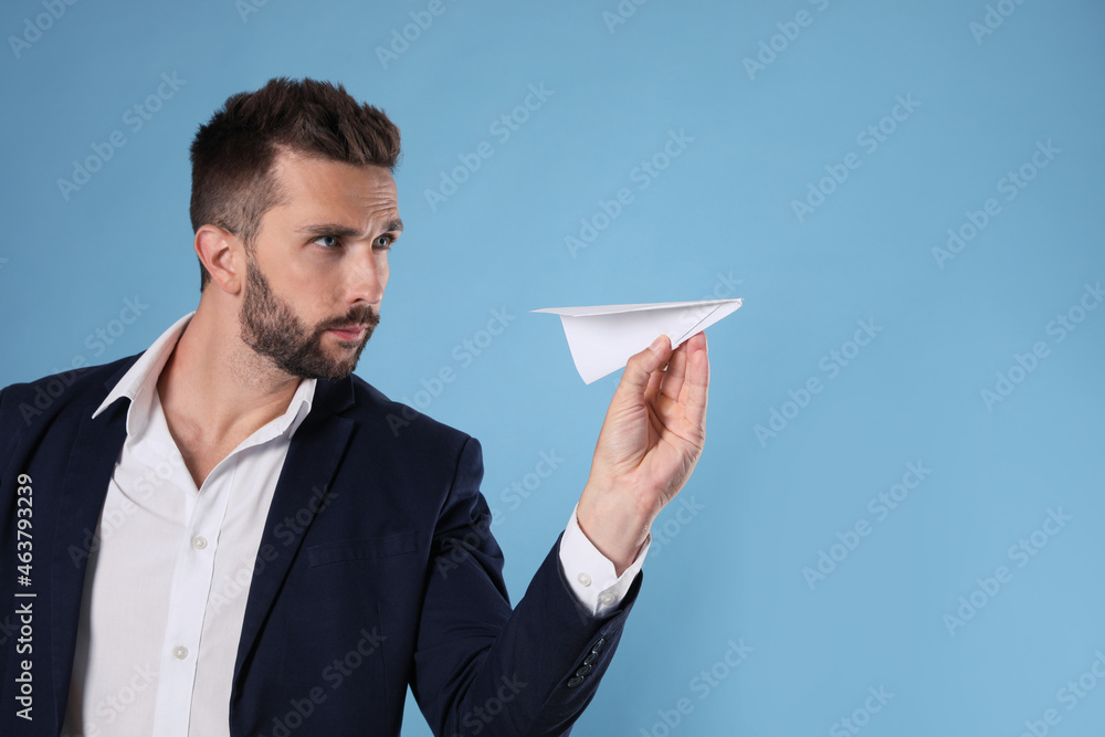 Handsome businessman playing with paper plane on light blue background. Space for text Handsome businessman playing with paper plane on light blue background. Space for text