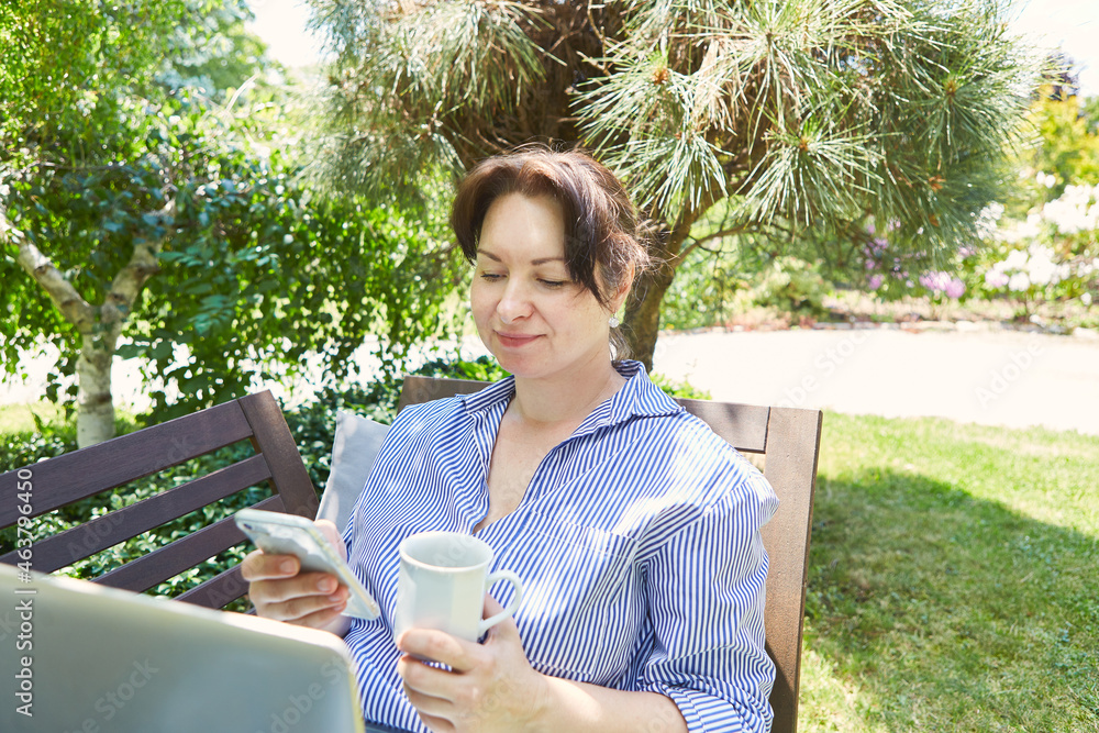 Frau versendet SMS mit Smartphone im grünen Garten Frau versendet SMS mit Smartphone im grünen Garten