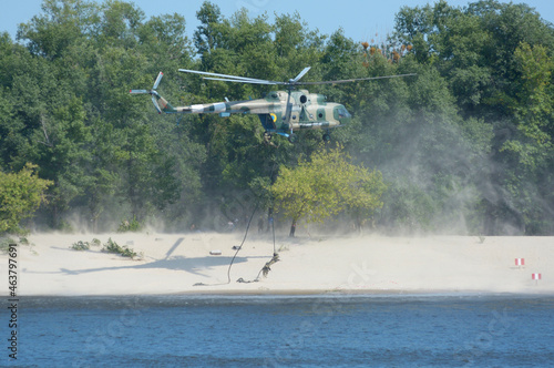 Military helicopter disembarking soldiers of Seaborne special forces on sandy beach attacking enemy, training photo