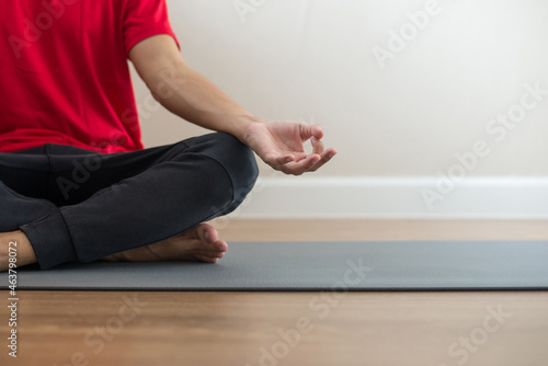 A young Asian man wearing a red workout shirt sits on a yoga mat. He was sitting with his eyes closed, meditating, practicing meditation. He likes to exercise with yoga, it relieves him from stress.