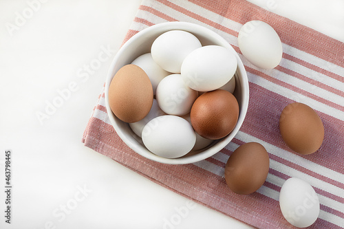 Chicken eggs in a white bowl. Ingredient for breakfast on a cotton napkin. Top view, flat lay. Selective focus.