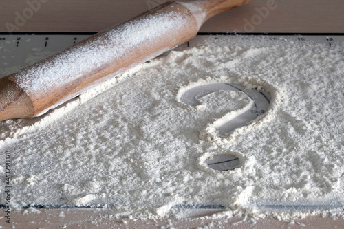 Question mark on the background of flour. What to cook dinner? Concept question  home baking. Question mark drawn on scattered flour on table with wooden rolling pin.