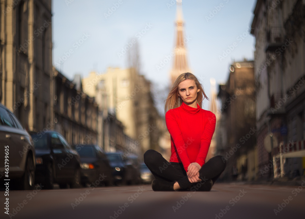 Thoughtful blonde in a red turtleneck sits on the road against the backdrop of the urban Thoughtful blonde in a red turtleneck sits on the road against the backdrop of the urban