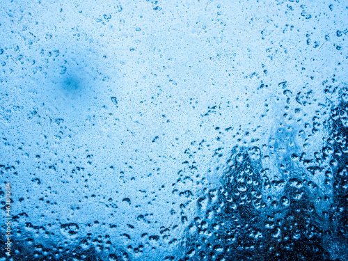 Water droplets on a surface, with a dark blue and scary view behind the glass. 