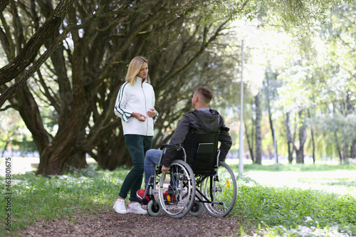 Young woman communicates with man in wheelchair in park