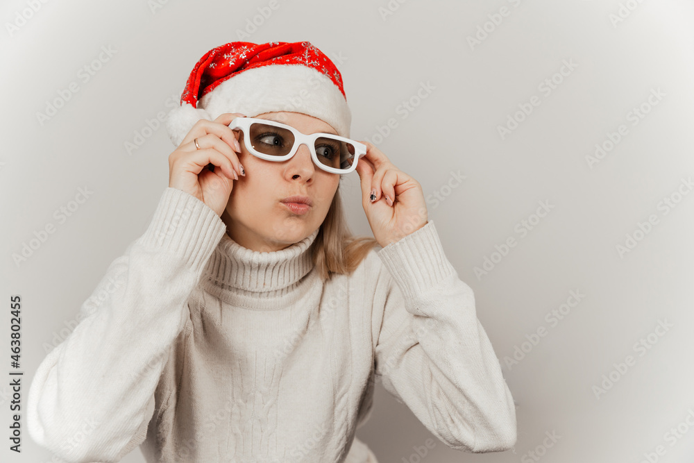 Portrait of cute smiling girl in white sweater, santa hat and glasses on gray isolated background Portrait of cute smiling girl in white sweater, santa hat and glasses on gray isolated background