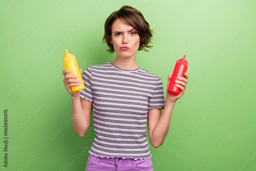 Photo of mad young brunette lady press ketchup mustard wear striped t-shirt isolated on green color background Photo of mad young brunette lady press ketchup mustard wear striped t-shirt isolated on green color background