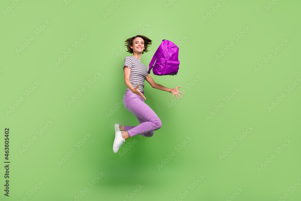 Photo of pretty shiny young woman dressed striped t-shirt throwing backpack jumping smiling isolated green color background Photo of pretty shiny young woman dressed striped t-shirt throwing backpack jumping smiling isolated green color background