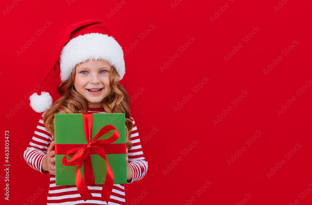 Christmas banner child in a santa hat holding a gift on a red background with place for text Christmas banner child in a santa hat holding a gift on a red background with place for text