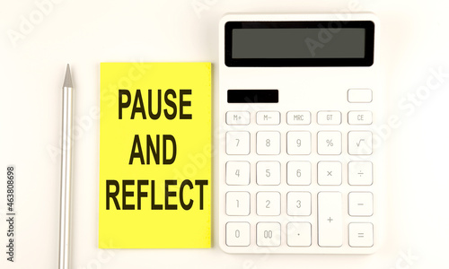 text PAUSE AND REFLECT on yellow sticker, next to pen and calculator