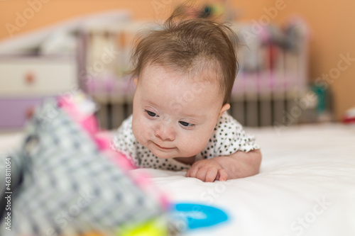 Baby Girl with Down Syndrome Stand on your belly and looking at a toy