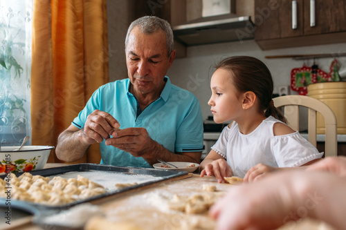 family traditions, grandfather and granddaughter make dumplings together at the table, grandfather helps granddaughter