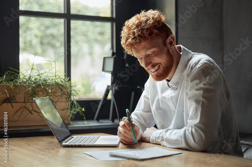 Fotografija Young red head man using notebook at wooden desk
