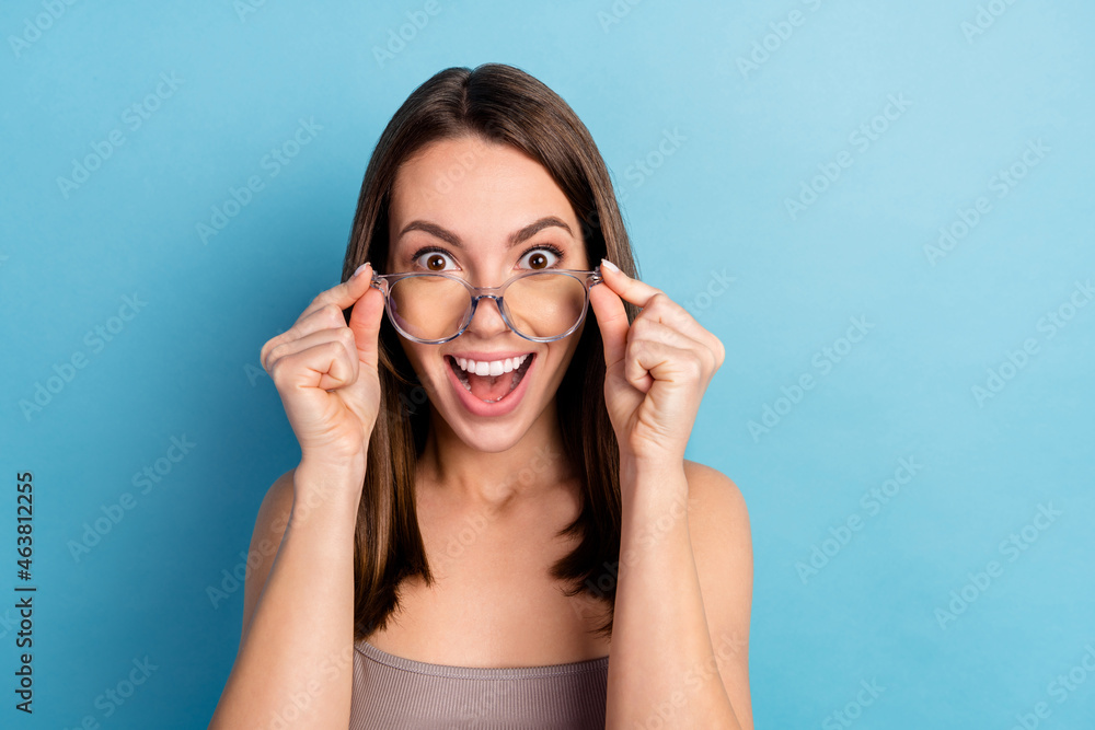 Photo of young girl happy positive smile amazed shocked hands touch eyeglasses look isolated over blue color background Photo of young girl happy positive smile amazed shocked hands touch eyeglasses look isolated over blue color background