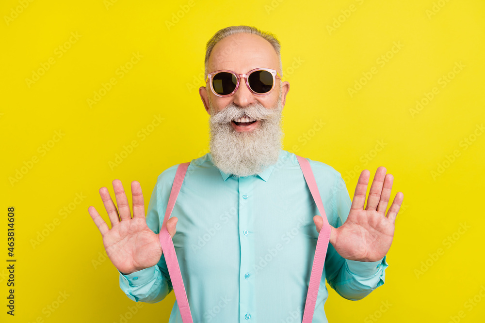 Naklejka premium Photo portrait of elder man in teal shirt sunglass laughing touching suspenders isolated on bright yellow color background