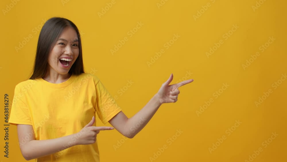 Cheerful Asian Lady Pointing Fingers Aside Nodding Head, Yellow Background Cheerful Asian Lady Pointing Fingers Aside Nodding Head, Yellow Background