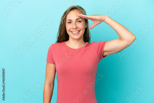 Young caucasian woman isolated on blue background saluting with hand with happy expression