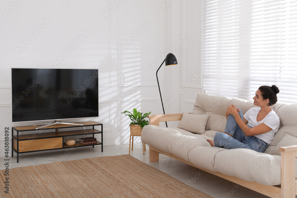 Woman watching television at home. Living room interior with TV on stand - obrazy, fototapety, plakaty 