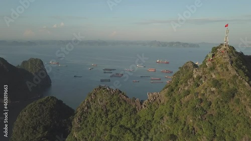 High hill with TV tower on top covered with greenery against traditional fishing boats sailing in sea bay aerial view Ha Long Vietnam