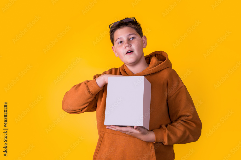 handsome boy with glasses in a brown sweatshirt holding a box on a yellow background handsome boy with glasses in a brown sweatshirt holding a box on a yellow background