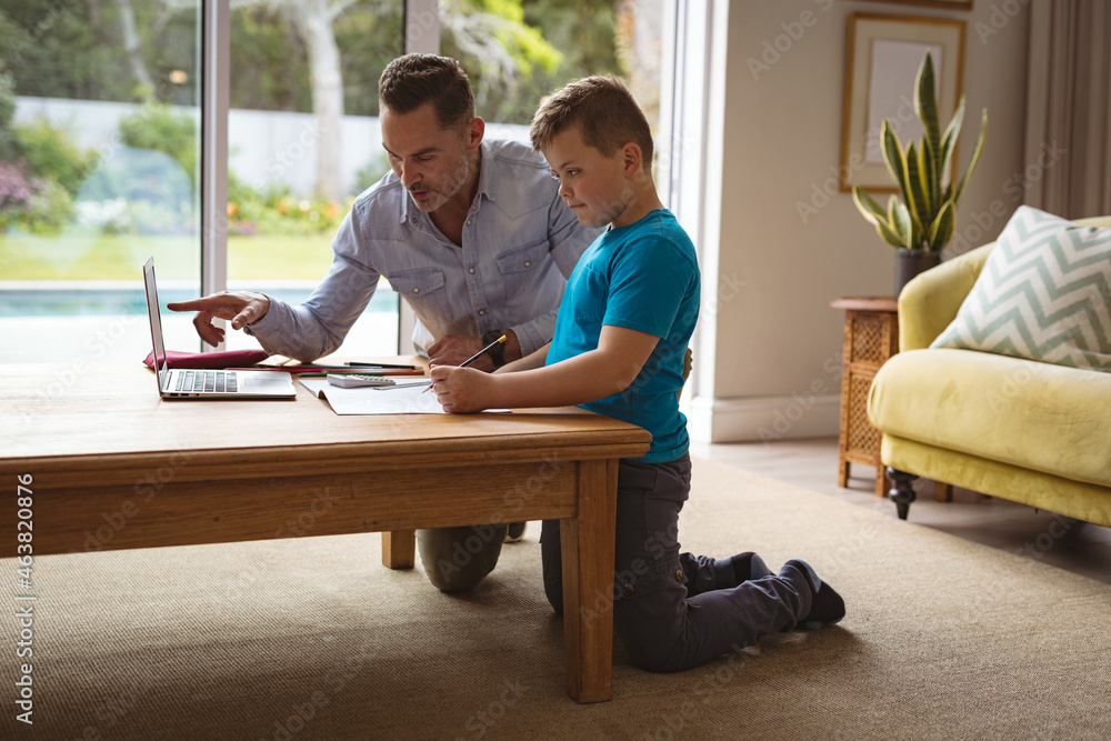 Caucasian father using laptop to help his son with homework at home Caucasian father using laptop to help his son with homework at home