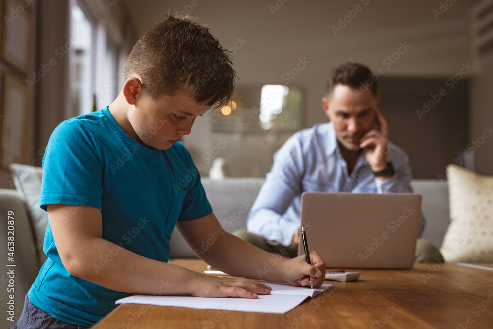 Caucasian father using laptop while son doing his homework at home Caucasian father using laptop while son doing his homework at home