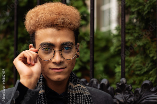 Portrait of handsome young black man with heterochromia wearing round eyeglasses outdoors (selective focus on eyes) photo