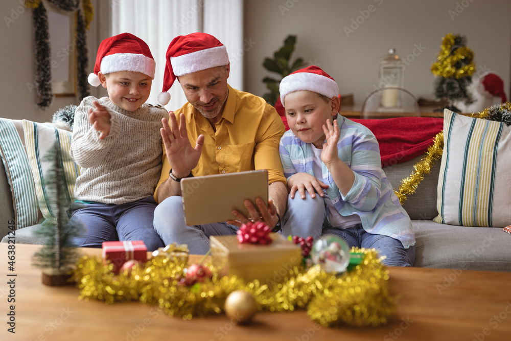 Caucasian father and two sons having a video call on digital tablet at home during christmas