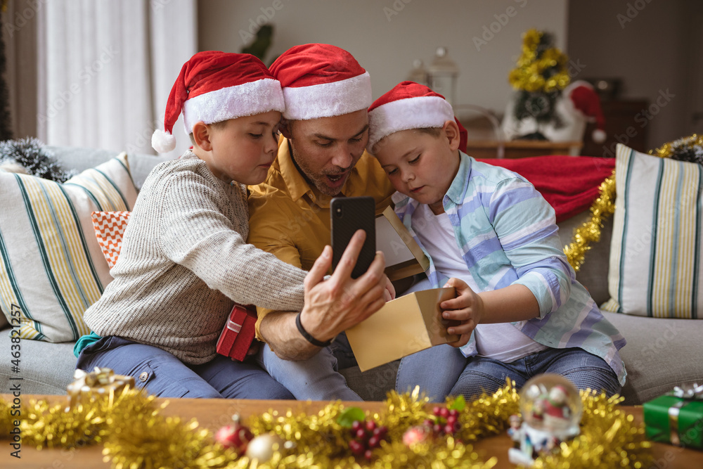 Caucasian father and two sons opening gift box during video call on smartphone during christmas Caucasian father and two sons opening gift box during video call on smartphone during christmas
