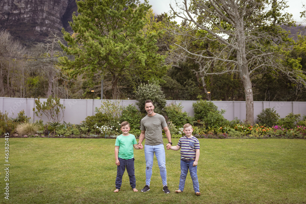 Portrait of caucasian father and two sons holding hands smiling while standing in the garden Portrait of caucasian father and two sons holding hands smiling while standing in the garden