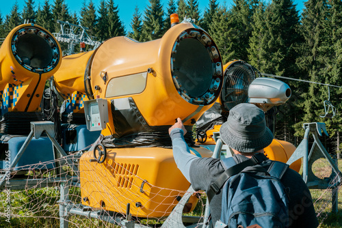 Repair man shows point finger on a snow making machine in the wood. Huge device. Control. Check. Nature. Electricity. Power