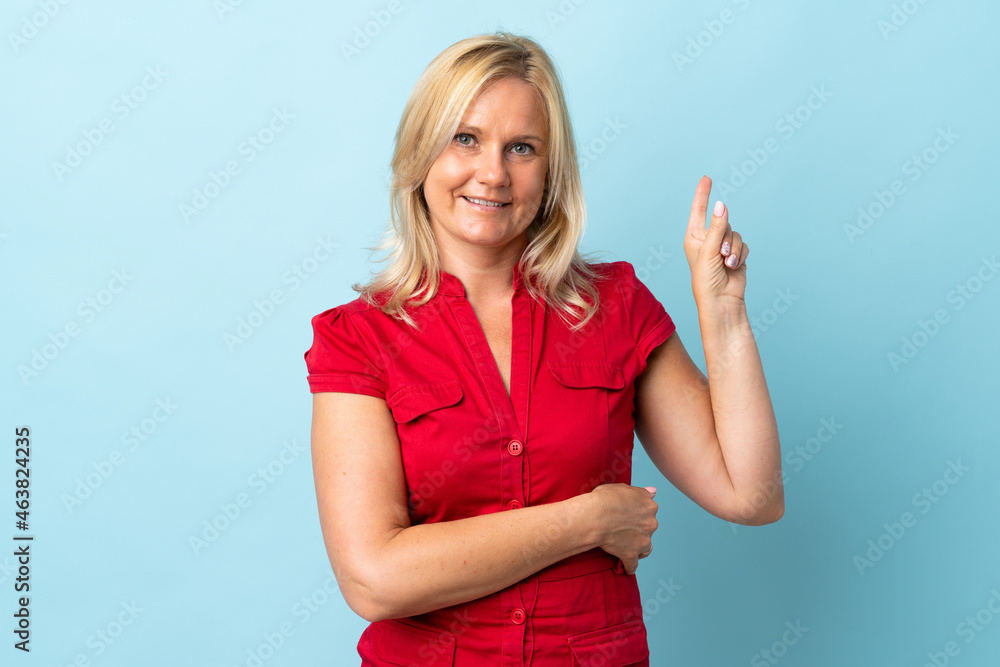 Fototapeta premium Middle age woman isolated on blue background showing and lifting a finger in sign of the best