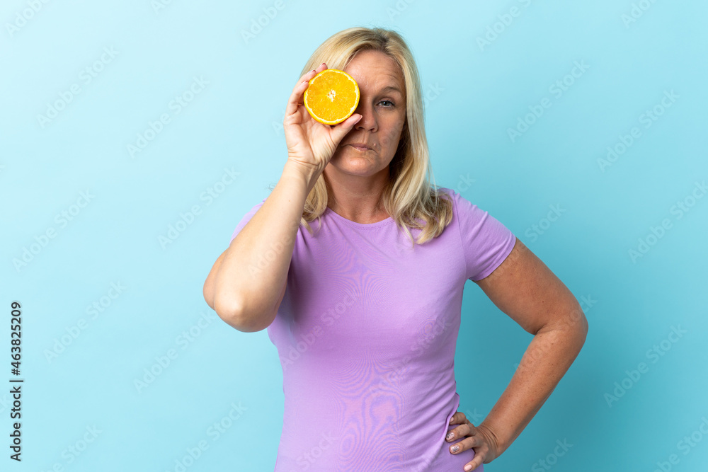 Middle age Lithuanian woman isolated on blue background holding an orange Middle age Lithuanian woman isolated on blue background holding an orange