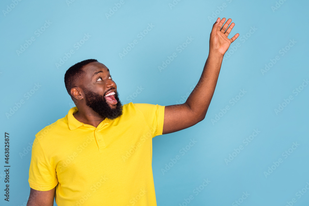 Photo of impressed sweet dark skin guy dressed yellow t-shirt holding arms looking empty space isolated blue color background