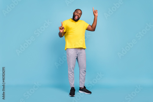 Photo of pretty sweet dark skin guy dressed yellow t-shirt smiling pointing fingers empty space isolated blue color background