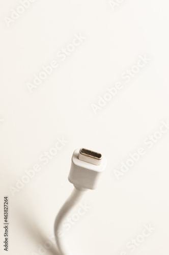 A white USB C cable and connector standing on a white surface, creating a light grey shadow. Vertical image with blank white space on top half