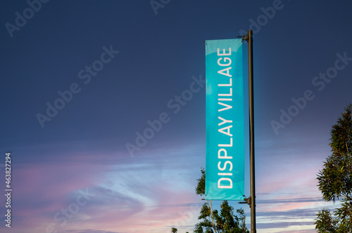 Blue vertical ‘display village’ banner in-front of an overcast blue and purple sunset in suburbia