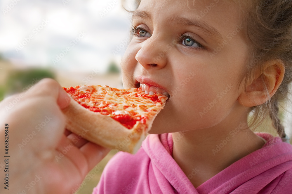 little girl eats pizza close up from parent's hand little girl eats pizza close up from parent's hand