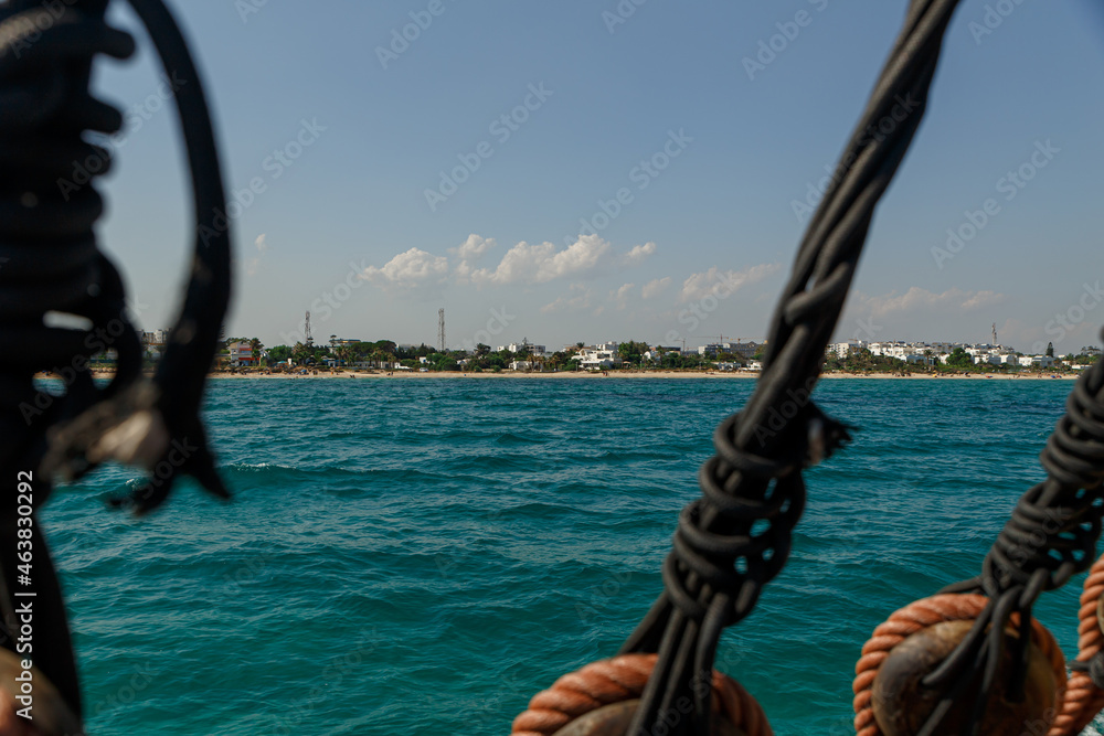 Obraz premium View of the Mediterranean coastline with blue water through the rigging of a sea vessel. Cyprus. Rest at the sea. Cruise