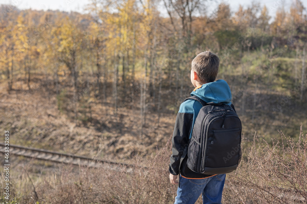 Teenager boy with backpack walking on path in autumn park. Active lifestyle, Back to school. Rear view of student boy in fall forest. People from behind Teenager boy with backpack walking on path in autumn park. Active lifestyle, Back to school. Rear view of student boy in fall forest. People from behind