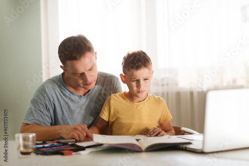 dad helps son schoolboy do lessons. homeschooling, distant learning. child boy is using a laptop and study online with video call teacher at home. 