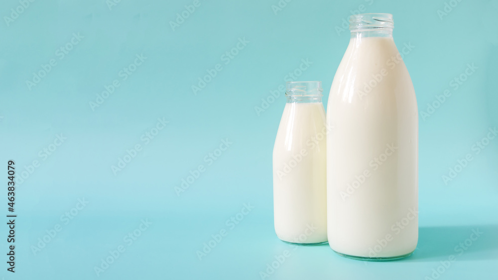 Two glass bottles of milk on a blue background. A liter and 0.5 liters of milk in glass bottles on a colored background a place for text Two glass bottles of milk on a blue background. A liter and 0.5 liters of milk in glass bottles on a colored background a place for text
