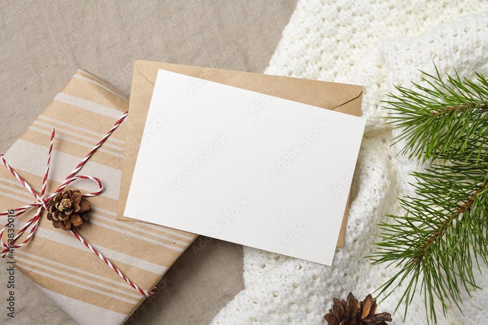 Christmas greeting card mockup with envelope, gift box and pine tree branch with cones on knitted background