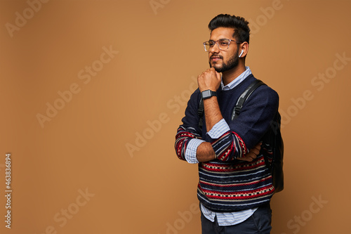 Thinking smart indian student with crossed arms standing on background with copy space
