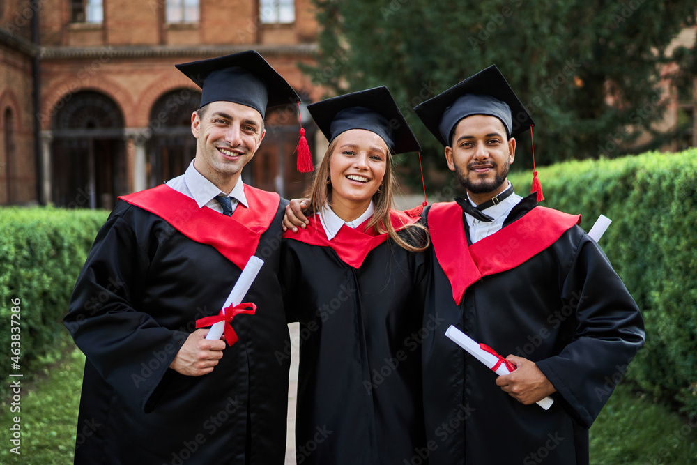 Portrait of three smiling graduate friends in graduation robes in